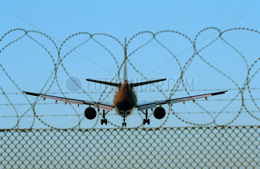 Flugzeug im Landeanflug hinter einem Stacheldrahtzaun
