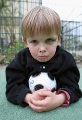 Berlin  Deutschland  kleiner Junge mit Fussball schaut traurig zum Betrachter