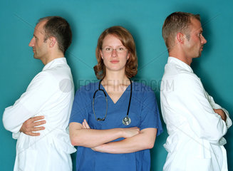 Eine Medizinerin steht zwischen zwei Aerzten in Kitteln