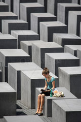 Berlin  Deutschland  eine junge Frau sitzt auf einer Stele im Stelenfeld  Holocaustmahnmal