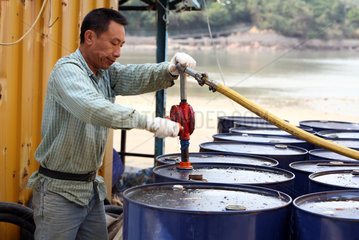 Hong Kong  China  Mann pumpt Diesel aus einer Blechtonne ab