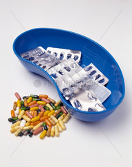 Tabletten liegen neben einer blauen Nierenschale mit leeren Blisterpackungen