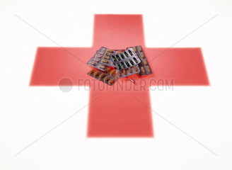 Tabletten in Blisterpackungen liegen auf einem symbolisierten roten Kreuz