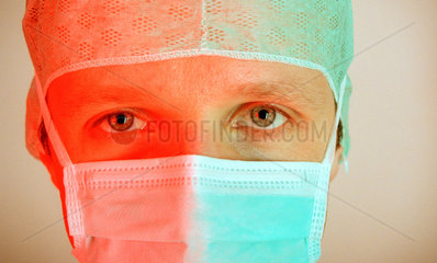 Portrait eines Arztes mit Mundschutz und OP-Haube in rot-gruenem Licht