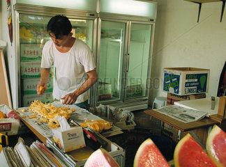 Ein junger Mann in einem kleinen Obstgeschaeft in Singapur