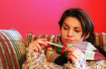 Eine kranke Frau liest vom Fieberthermometer ab