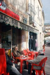 Oristano  Italien  drei Maenner sitzen auf roten Plastikstuehlen vor einem Cafe