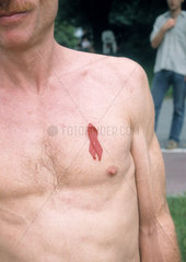 Mann mit nacktem Oberkoerper traegt die Rote AIDS-Schleife
