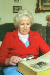 Eine alte Frau liest mit einer Lupe in einer Bibel.