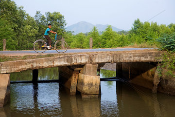 Kampot  Kambodscha  ein Junge auf einem Fahrrad ueberquert eine Bruecke