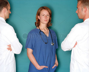 Eine Medizinerin steht zwischen zwei Aerzten in Kitteln