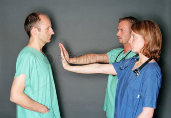 Zwei Mediziner mit distanzierender Geste zu einem Dritten