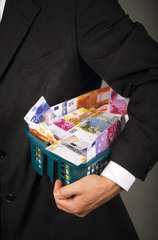 Mann im Anzug haelt Waeschekorb voller Eurogeldscheine