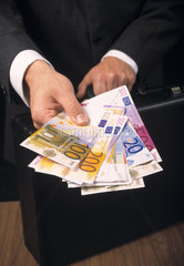 Mann in Anzug mit Aktenkoffer haelt Eurogeldscheine in der Hand