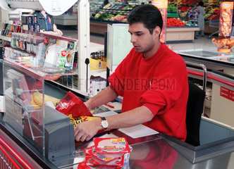 Junger Mann arbeitet an der Kasse eines Supermarktes.