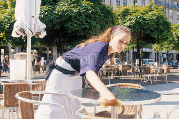 Junge Mitarbeiterin eines Strassencafes reinigt Tische