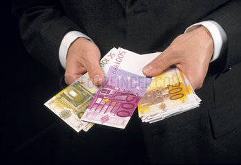 Mann im Anzug haelt Eurogeldscheine in seinen Haenden