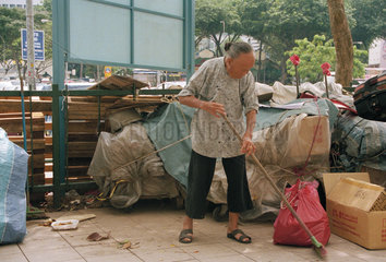 Eine alte Frau zwischen Muellsaecken in Singapurs Chinatown