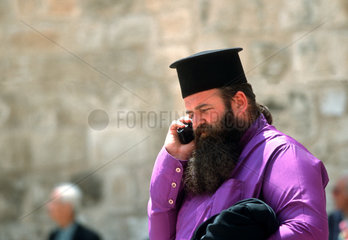 Orthodoxer Priester telefoniert mit einem Handy.