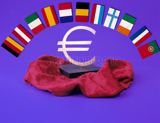 Der Euro auf einem Sockel mit rotem Samt darunter  darueber die elf Flaggen der Eurolaender