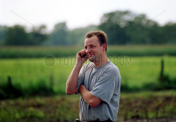 Junger Landwirt mit Handy auf dem Feld