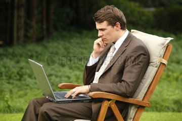 Deutschland  ein junger Mann im Anzug sitzt im Garten an seinem Laptop