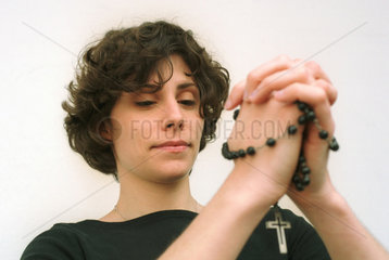 Eine junge Frau betet mit einem Rosenkranz.