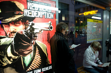 Berlin  Deutschland  ein lesender Mann vor der Werbung fuer den Western-Shooter Red Dead Redemption