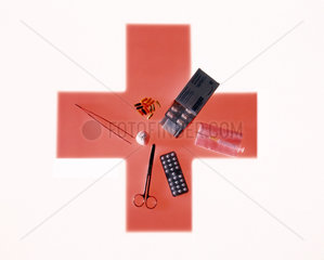 Diverse medizinische Utensilien liegen auf einem roten Kreuz als Symbol darunter