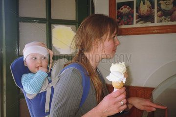 Eine Frau in der Eisdiele mit ihrem Kind in der Rueckentrage