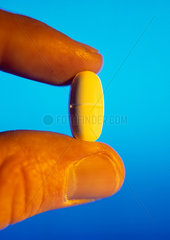 Tablette mit Antibiotika in zwei Fingern gehalten mit farbigem Licht
