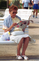 Eine Frau auf der Strandprommenade beim Zeitungslesen