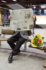 Mann liest Zeitung auf dem Flughafen Zuerich Klothen