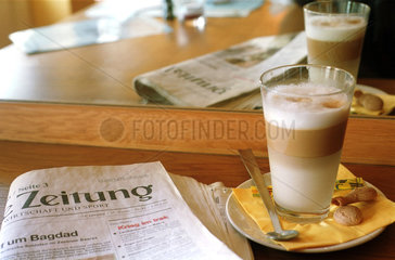 Eine Zeitung liegt neben einem Glas Latte Macchiato.