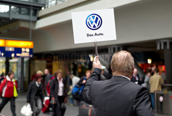 Berlin  Deutschland  Mann haelt ein Schild mit VW-Logo hoch