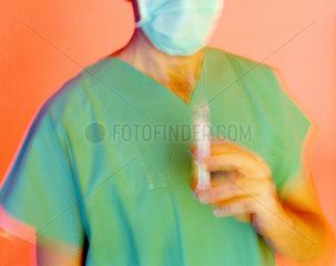 Mediziner mit Mundschutz und einer Spritze in der linken Hand