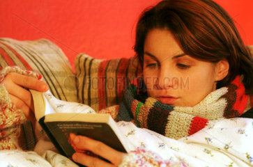Eine junge Frau liest warm zugedeckt ein Buch