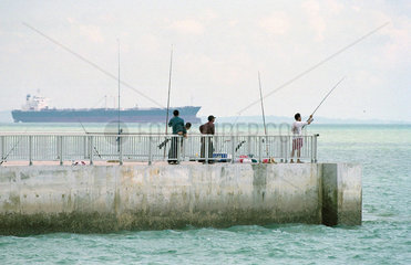 Angler auf einer Mole an der Kueste Singapurs  im Hintergrund ein Frachtschiff