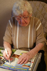 Eine Rentnerin raetselt in einer Raetselzeitung