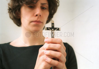 Eine junge Frau betet mit einem Kruzifix.