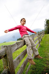 Tirol  ein Maedchen balanciert im Sitzen auf einem Zaun