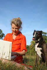 Berlin  Deutschland  eine Frau sitzt mit ihrem Laptop auf der Wiese  daneben ihr Hund