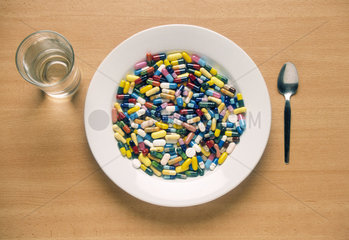 Ein Teller gefuellt mit Tabletten  daneben ein Glas Wasser und ein Loeffel