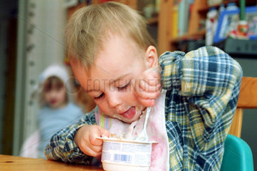 Ein Junge sitzt am Tisch und isst einen Joghurt