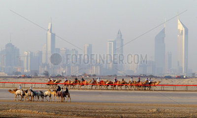 Kamele und Reiter in der Wueste vor der Skyline von Dubai