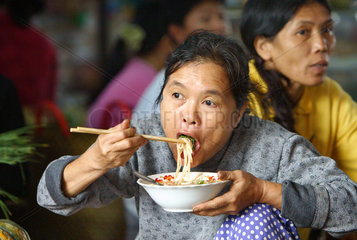 Vietnam  Marktfrau isst ein asiatisches Nudel-Gericht mit Staebchen