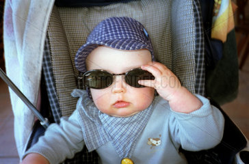 Kind im Kinderwagen mit einer Sonnenbrille