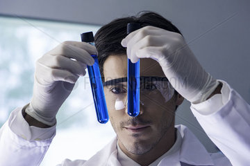 Researcher scrutinizing test tubes containing blue liquid in lab