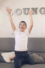 Boy playing on sofa with arms raised in the air