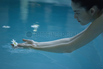 Woman reaching for flower floating in pool